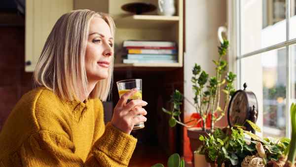 Mature woman drinking glass of water in the kitchen looking through the window