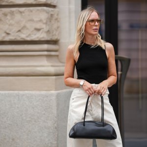 MUNICH, GERMANY - JULY 3: Mirja Klein is seen wearing a black high neck cotton tanktop from COS; washed white Ines denim trousers with fold-over closure and wide leg silhouette from DARKPARK; a black Eastside leather bowling bag with elongated shape from COS; transparent sunglasses with slightly brown colored acetate frame and glasses in rectangular shape from Saint Laurent; a vintage silver-golden bicolor Santos de Cartier wristwatch from Cartier on July 3, 2025 in Munich, Germany. (Photo by Moritz Scholz/Getty Images)