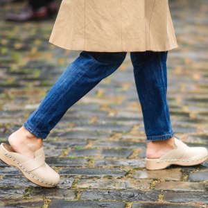 PARIS, FRANCE - JUNE 26: A guest wears a long beige trench coat, blue flared denim jeans pants, beige nailed / studded mules shoes, outside Hermes, during Paris Fashion Week - Menswear Spring/Summer 2022, on June 26, 2021 in Paris, France. (Photo by Edward Berthelot/Getty Images)
