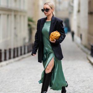 PARIS, FRANCE - JANUARY 25: Justyna Czernia wears sunglasses, gold earrings, a green mint satin silk slit / split long dress, a black oversized blazer jacket, an orange shiny leather puffy handbag from Bottega Veneta, black shiny leather pointed high boots, gold ring, outside Alexis Mabille, during Paris Fashion Week - Haute Couture Spring/Summer 2022, on January 25, 2022 in Paris, France. (Photo by Edward Berthelot/Getty Images)