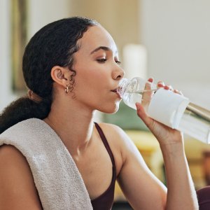 Woman, exercise and drinking water on floor in home with thinking, hydration or liquid for health detox. Girl, person and bottle for workout, nutrition and wellness with training for fitness in house