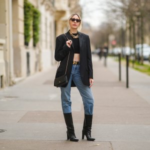 PARIS, FRANCE - FEBRUARY 22: Emy Venturini wears sunglasses, golden earrings, a golden large chain necklace, a black cropped top from Elisabetta Franchi, a black oversized blazer jacket, a Hermes belt, a black leather Chanel bag, blue denim jeans 501 Levi's, black high heeled pointy leather high boots, on February 22, 2021 in Paris, France.
