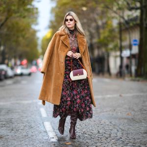 Kate Tik wears black sunglasses, a black with red / purple / green flower print pattern turtleneck transparent long sleeves t-shirt form Misa Los Angeles , a matching black with red / purple / green flower print pattern high waist long skirt from Misa Los Angeles, a brown oversized fluffy long coat from Stand Studio, multicolored pearls bracelets, gold rings, a burgundy / camel / white latte matte leather yoke handbag from Noirgaze, brown shiny leather pointed heels knees boots from Neil J Rogers, during a street style fashion photo session, on October 31, 2021 in Paris, France.