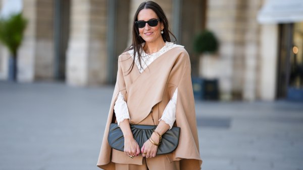 Alba Garavito Torre wears black sunglasses from Ray Ban, white large pearls earrings, a white shirt with cut-out lace pattern large collar, a beige felt / wool oversized cloak, matching beige wool / felt palazzo pants, a black shiny leather ruffled handbag, a gold Love bracelet from Cartier, gold bracelet, gold rings, during a street style fashion photo session, on October 28, 2021 in Paris, France.