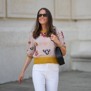 Alba Garavito Torre wears black sunglasses from Ray Ban, gold earrings, a gray with red / yellow / navy blue braided flower embroidered pattern / puffy short sleeves t-shirt, white high waist denim jeans pants from Mother Denim, black shiny leather Timeless shoulder bag from Chanel, during a street style fashion photo session, on June 06, 2023 in Paris, France.