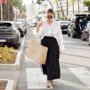 CANNES, FRANCE - MAY 15: Gili Biegun wears black long maxi skirt, white long sleeve shirt, oversized beige straw bag, sunglasses and sea shell golden earrings during day three of the 78th Cannes Film Festival on May 15, 2025 in Cannes, France. (Photo by Raimonda Kulikauskiene/Getty Images)