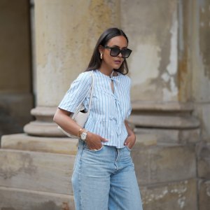 HAMBURG, GERMANY - MAY 7: Laura Noltemeyer is seen wearing a light indigo blue wide leg jeans from Agolde, a cotton puff sleeve blouse with ties in the front in white with blue stripes from Sézane, black oversized cat-eye acetate sunglasses from Celine, Arco handbag in white intrecciato leather from Bottega Veneta, big golden drop-shaped earrings, a small Lady-Datejust watch in gold-silver from Rolex, a golden LOVE bracelet from Cartier, stacked golden rings from Cartier on May 7, 2025 in Hamburg, Germany. (Photo by Moritz Scholz/Getty Images)