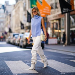 LONDON, ENGLAND - SEPTEMBER 15: Xenia Adonts wears sunglasses, a blue wool sleeveless turtleneck pullover, white pants, a bag featuring several attached squares, white boots, during London Fashion Week September 2019 on September 15, 2019 in London, England. (Photo by Edward Berthelot/Getty Images)