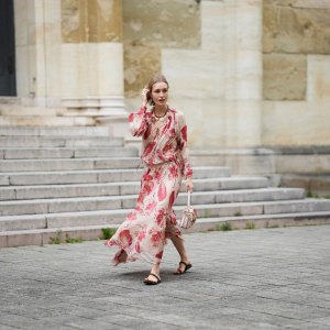 MUNICH, GERMANY - MAY 29: Marlies Pia Pfeifhofer is seen wearing a light beige silk chiffon long sleeve maxi dress with red and pink prints of feathers and flowers, drawstring waist, deep V-neck with front tie and smocking details on the collar and cuffs from FENDI, a natural-colored Baguette canvas bag with coral bandana embroidery, small fringes on the flap, calfskin leather straps, golden hardware and logo detail as well as an additional golden chain metal charm with marine-inspired pendants and a red, pink and white bandana charm with golden logo clip from FENDI, a pair of chocolate brown leather gladiator sandals with a braided leather toe strap and one main strap from Alex Rivière x Manebi, a gold-colored metal and brown nappa leather Forever Fendi necklace with shell-shaped pendants from FENDI, a yellow golden Leaves ring from Ole Lynggaard on May 29, 2025 in Munich, Germany. (Photo by Moritz Scholz/Getty Images)