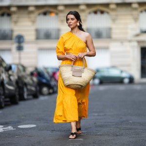 PARIS, FRANCE - AUGUST 12: Ketevan Giorgadze @katie.one wears a one shoulder cut out maxi dress in orange from Mango, oversized golden hoop earrings from Zara, flip flop heeled black sandals shoes from APC Paris, a Le Grand Panier beach straw bag by Jacquemus, on August 12, 2021 in Paris, France. (Photo by Edward Berthelot/Getty Images)