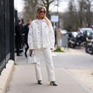 PARIS, FRANCE - MARCH 09: A guest wears dark brown sunglasses, white t-shirt, gold layered necklaces, cream oversized denim jean Lacoste jacket, cream loose denim jean cuffed Lacoste pants, shiny white Lacoste leather bag, dark green heeled leather shoes, outside Lacoste, during the Paris Fashion week Women's Fall/Winter 2025-2026 on March 9, 2025 in Paris, France. (Photo by Edward Berthelot/Getty Images)
