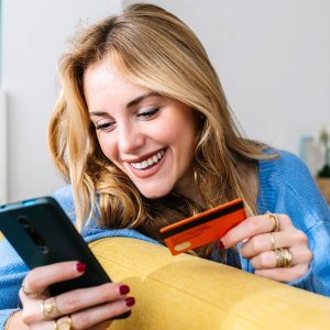 Happy young woman holding credit card while shopping online at home - stock photo