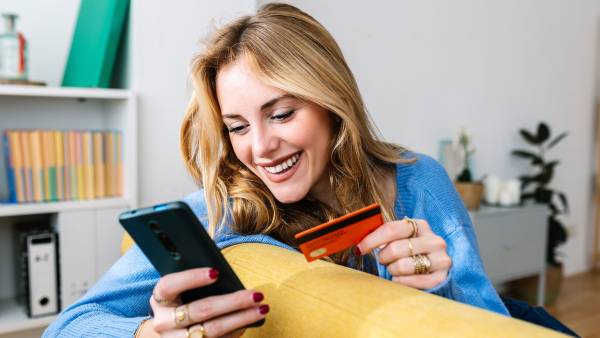 Happy young woman holding credit card while shopping online at home - stock photo