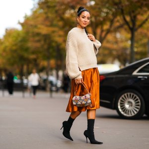 PARIS, FRANCE - SEPTEMBER 28: Tamara Kalinic wears a wool pullover, an orange shiny silky skirt, earrings, a Fendi bag, black high heeled boots, outside CDG Comme des Garçons, during Paris Fashion Week - Womenswear Spring Summer 2020 on September 28, 2019 in Paris, France. (Photo by Edward Berthelot/Getty Images)
