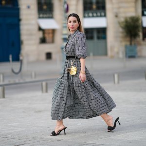Maria Rosaria Rizzo @lacoquetteitalienne wears earrings, a grey gathered checked dress with puff sleeves from Parosh, a golden bracelet, a golden mini bag from Duren Japan, black leather sandals shoes from LPA, golden jewelry from & Other Stories, on March 03, 2021 in Paris, France.