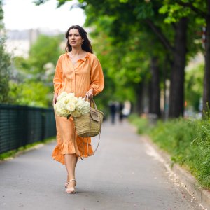 PARIS, FRANCE - MAY 10: Ketevan Giorgadze @katie.one wears gold earrings, a long buttoned coral loungewear linen The Sleeper dress with puffy sleeves, gold rings, a wicker with brown shiny leather detail Le Panier Soleil Jacquemus tote-bag, white strappy low heeled Raye sandals, on May 10, 2021 in Paris, France. (Photo by Edward Berthelot/Getty Images)