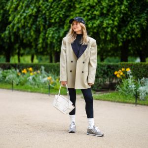 PARIS, FRANCE - MAY 27: Xenia Adonts wears a black cap from Museum of Peace and Quiet, a black ribbed turtleneck pullover, a beige long oversized jacket from Attire The Studio, black leggings from Nike, a white matte leather Bottega Veneta handbag, white socks, gray sneakers from New Balance, gold pink rings, on May 27, 2021 in Paris, France. (Photo by Edward Berthelot/Getty Images)
