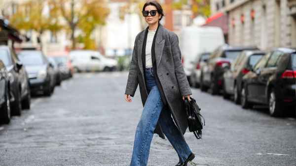 Katie Giorgadze @katie.one wears black sunglasses, a white latte ribbed high neck wool pullover, a black long blazer jacket, a black and white print pattern long oversized wool coat, high waist blue denim large ripped pants, a black shiny leather crocodile print pattern shoulder bag from Balenciaga, black shiny leather block heels loafers from Prada, on November 26, 2021 in Paris, France.