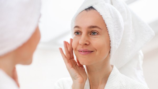 Happy 40s middle aged woman model touching face skin looking in mirror reflection. Smiling adult lady pampering, healthy moisturized skin care, aging beauty, skin care treatment cosmetics concept