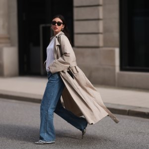HAMBURG, GERMANY - FEBRUARY 23: Milena Karl seen wearing Ray-Ban black Wayfarer sunglasses, silver earrings, Hermès silver chain / necklace, The Row beige oversized long coat, NA-KD blue denim wide leg jeans / pants, COS white cotton basic shirt, Alaia black leather heart shaped crossbody bag and Ganni beige snake pattern leather heeled boots, on February 23, 2024 in Hamburg, Germany. (Photo by Jeremy Moeller/Getty Images)