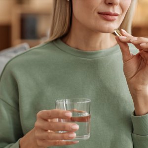 Minimal close up of adult woman taking vitamin pill and holding glass of water at home copy space