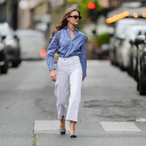 Segolene Hyppolite wears sunglasses, a blue and white oversized shirt from Tommy Hilfiger, a raffia beige bag from Vanessa Bruno, high waist white denim pants from Vanessa Bruno, Chanel slingback shoes in blue denim with black tips, during a street style fashion photo session, on May 20, 2024 in Paris, France.