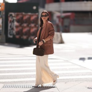 Yana Echko seen wearing YSL brown sunglasses, Bottega Veneta brown leather earrings, white pearl necklace, The Frankie Shop brown pinstripe vest, Express light brown corduroy blazer jacket, Reformation cream white maxi silk long skirt, MARGE SHERWOOD brown suede leather small bag, Kenneth Jay Lane gold ring, cream white / brown bangle and JW Anderson white leather pumps, outside the Bach Mai show, during the New York Fashion Week, on September 08, 2024 in New York City.