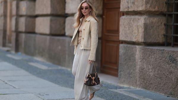 Sonia Lyson is seen wearing oval cat-eye sunglasses with brown lenses and a thin silver metal frame from Prada; several earrings and stud earrings; a fine gold necklace with a round pendant; a beige suede jacket with large collar and white decorative seams from Zara; a light brown ribbed top with high round neckline from Munthe underneath; a brown leather “Odyssee“ handbag from Louis Vuitton; wide-leg cream-white pants from Zara; and beige suede heeled sandals, also from Zara on June 20, 2025 in Berlin, Germany.