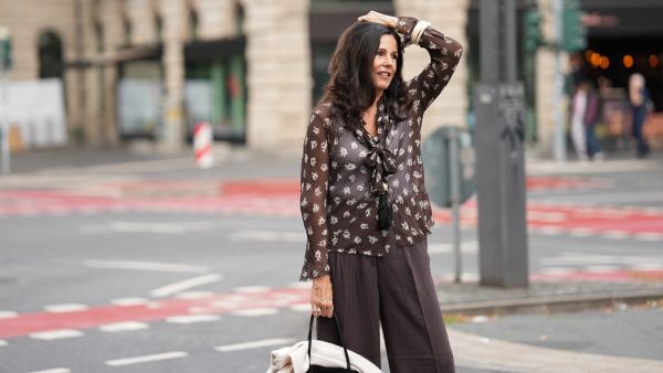 Angelika Hanel is seen wearing a chocolate brown flowing shirt with scarf collar, semi-sheer fabric, cream white floral print and button-up front from Massimo Dutti; a soft beige v-neck cashmere pullover with a relaxed silhouette and subtle ribbed cuffs and hem from Sa Su Phi; dark brown wide-leg linen blend trousers with a relaxed fit from H&M; a large black suede top-handle Soft Margaux 17 bag with softly structured sides, gold-tone buckles on the sides and a curved silhouette from The Row; a long black ceramic tassel cord necklace from Massimo Dutti; a golden necklace with a vintage Alhambra pendant in the shape of a cloverleaf from Van Cleef & Arpels; a golden Day-Date wristwatch from Rolex; a white gold pavé diamond tennis bracelet; an ecru colored Luca arm cuff set of two, made of synthetic resin from Sézane; a ring stacked with gold bands and a diamond from Marré; a diamond ring on July 27, 2025 in Frankfurt am Main, Germany.