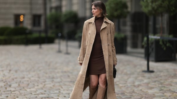 Yana Pries seen wearing a long suede leather trench coat from NOUR HAMMOUR in a warm beige tone. The coat features double-breasted buttons, a structured collar, and belted cuffs, creating a luxurious yet timeless silhouette. Her hair is cut into a sleek bob, light brown with subtle highlights, styled with a middle part and softly curved ends that frame her face. Underneath she wears Even&Odd fitted chocolate-brown mini dress, with a high neckline, Bottega Veneta Andiamo clutch, a structured black leather bag with a gold knot detail on the strap and Bobbies knee-high Bobbies suede leather boots in a soft beige tone, on September 17, 2025 in Berlin, Germany.