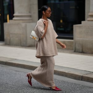 HAMBURG, GERMANY - SEPTEMBER 19: Cherifa Akili is seen wearing an oversized beige short-sleeve knit sweater with a soft texture from Byaylinkönig; a matching long knit skirt in a beige tone with subtle seaming at the hem from Byaylinkönig; red pointed-toe heels with a low cut from Prada; The Constance structured white leather shoulder bag with a gold clasp from Hermes; a gold spiral shaped bracelet from Elouise; two gold, metallic rings from Elouise, Wempe; lightly tinted sunglasses in a warm shade COS; her black hair is pulled back in a sleek bun on September 19, 2025 in Hamburg, Germany. (Photo by Moritz Scholz/Getty Images)