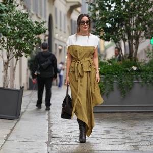 MILAN, ITALY - SEPTEMBER 27: Tamara Kalinic wears long dark brown hair styled in a low loose ponytail with a center part, black rectangular sunglasses, a gold choker-length necklace with matching gold bracelet and rings, a brown suede top-handle satchel bag, a mustard yellow patterned midi dress with a white shoulder yoke and capped sleeves, a self-tie waist belt and an asymmetrical handkerchief hem in a lightweight woven fabric, dark brown leather knee-high boots with a stacked high heel, outside Ferragamo, during Milan Fashion Week - Womenswear Spring/Summer 2026, on September 27, 2025 in Milan, Italy (Photo by Edward Berthelot/Getty Images)