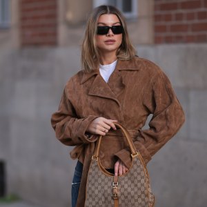 BERLIN, GERMANY - NOVEMBER 02: Sophia Geiss is seen wearing rectangular black sunglasses with a wide tapered temple from Prada; two different-sized gold hoop earrings and a gold stud earring; a silver nose ring; a brown suede jacket with large notch lapels, shoulder pads, decorative seams, a tie belt, and belted cuffs from & Other Stories; a white t-shirt underneath; a brown logo-embellished canvas bag with brown leather details and handles from Gucci; a silver ring; ans wide-legged dark jeans with orange decorative seams from Closed on November 02, 2024 in Berlin, Germany. (Photo by Jeremy Moeller/Getty Images)
