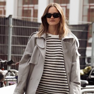 COPENHAGEN, DENMARK - AUGUST 04: A guest wears black and white stripped min dress, long black boots and grey trench coat outside Bonnetje show during Copenhagen Fashion Week day one on August 04, 2025 in Copenhagen, Denmark. (Photo by Raimonda Kulikauskiene/Getty Images)