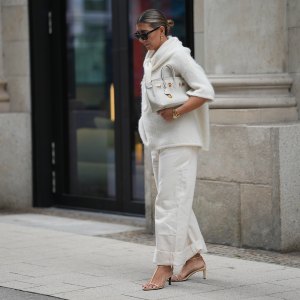 HAMBURG, GERMANY - SEPTEMBER 19: Aylin König is seen wearing a short-sleeved, fluffy textured, oversized sweater in off-white with a high, tied neckline; relaxed off-white jeans with a wide cuff at the hem; nude strappy heeled sandals; a medium-sized white leather handbag with gold hardware; black rectangular sunglasses; gold link earrings from Tiffany & Co HardWear Collection; detailed gold bracelets from Cartier; a watch with a metallic wristband and white clock face from Cartier; her dark hair is pulled back into a neat, low bun on September 19, 2025 in Hamburg, Germany. (Photo by Moritz Scholz/Getty Images)