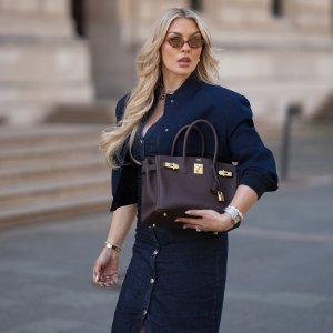 FRANKFURT AM MAIN, GERMANY - MAY 12: Paulina Kurka is seen wearing a navy blue cropped bomber jacket with big pockets from Zara, a denim midi dress with tailored waist and front button closure from Zara, light havana MU 04ZS sunglasses with round brown glasses and golden logo detail from Miu Miu, a chocolate brown Birkin 30 bag with golden details from Hermès, a silver triple wrap Farandole 120 fine link necklace with classic pendants from Hermès, silver hoop earrings, a medium sized silver Santos watch with square dial from Cartier, a silver Chaine d'ancre Enchainee chain bracelet from Hermès, a silver Chaine d'ancre Enchainee large model chain ring from Hermès, a custom-made diamond ring with square sapphire statement details, custom-made diamond engagement and wedding rings on May 12, 2025 in Frankfurt am Main, Germany. (Photo by Moritz Scholz/Getty Images)