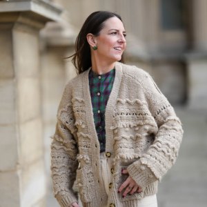 PARIS, FRANCE - MARCH 27: Alba Garavito Torre wears gold and green cross print pattern earrings, a green and purple checkered print pattern / puffy shoulder / buttoned shirt from Nina Blanc, high waist ivory high waist wide legs pants from Nina Blanc, a beige wool embroidered pattern oversized buttoned cardigan , during a street style fashion photo session, on March 27, 2023 in Paris, France. (Photo by Edward Berthelot/Getty Images)