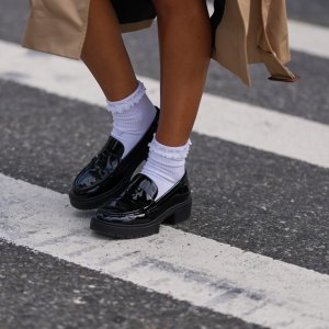NEW YORK, NEW YORK - SEPTEMBER 15: A guest wears a beige trench coat, black patent varnished leather chunky lug-sole loafers shoes worn with white crew socks, outside Coach, during New York Fashion Week, on September 15, 2025 in New York, New York (Photo by Edward Berthelot/Getty Images)