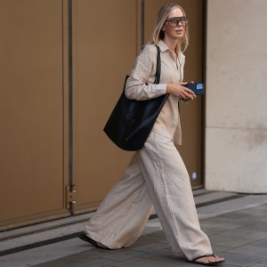 MUNICH, GERMANY - AUGUST 8: Mirja Klein is seen wearing a relaxed beige linen shirt with a pointed collar, hidden button-down front and long sleeves from Falconeri; wide-leg beige linen trousers with pleats from Falconeri; a pair of minimalistic rubber flat flip flop sandals from A.Emery; a large black leather medium Puzzle Fold Tote bag with geometric stitching, double shoulder straps and open-top design from Loewe; oversized square mask sunglasses with a tortoiseshell acetate frame and gradient lenses from Tom Ford on August 8, 2025 in Munich, Germany. (Photo by Moritz Scholz/Getty Images)