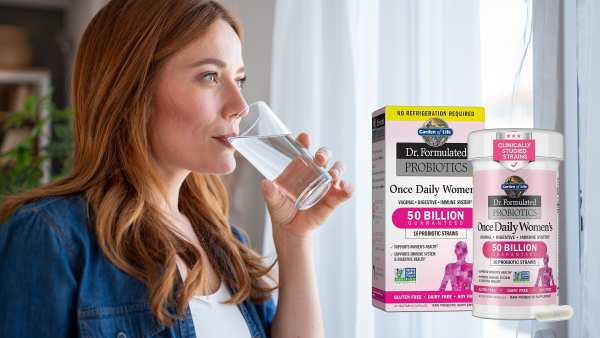 Mid adult woman enjoying a glass of fresh water while standing by the window at home, gazing outside and savoring a peaceful moment of relaxation and hydration