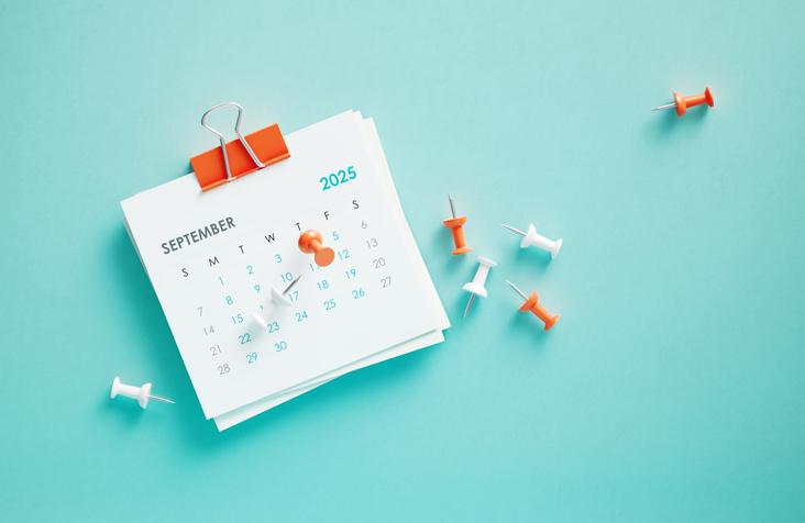 September 2025 calendar and thumbtacks on blue background. Horizontal composition. Reminder concept.