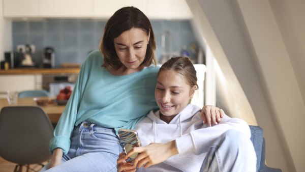 A mom and daughter spending time together, looking at a phone, in the living room. Photo by Catherine Delahaye/Getty Images