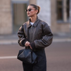 BERLIN, GERMANY - OCTOBER 12: Sophia Geiss is seen wearing oval rimless black sunglasses from Vehla Eyewear, two different-sized gold hoop earrings, a silver nose ring, a cropped dark brown leather jacket with wide sleeves and ribbed cotton cuffs from Meotine, a white top underneath, wide-legged dark vintage jeans with orange decorative seams, a silver ring, and a black leather bag with round handles from COS on October 12, 2024 in Berlin, Germany. (Photo by Jeremy Moeller/Getty Images)