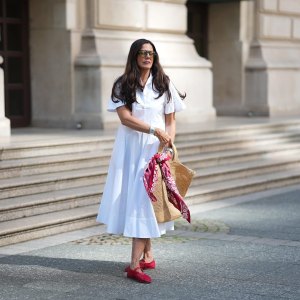 FRANKFURT AM MAIN, GERMANY - JULY 10: Angelika Hanel is seen wearing a white short-sleeved shirt midi dress with a flared silhouette and soft pleating from Erika Cavallini; a pair of signature Alaïa ballet flats in red fishnet textile and patent leather, a buckle strap on top and round toes from Alaïa; the ICARE maxi shopper crafted from hand-embroidered natural raffia and a brown gold oversized, sculptured Cassandre from Saint Laurent adorned with a red and white silk bandana from Arket tied to the handle; a silver Rolex Daytona watch; a yellow golden Juste un Clou bracelet from Cartier; a pavé diamond Tennis bracelet; a bold sterling silver Bone Cuff from Tiffany & Co.; oversized black aviator sunglasses with orange shaded glasses from Kapten & Son; long brown hair and natural make-up on July 10, 2025 in Frankfurt am Main, Germany. (Photo by Moritz Scholz/Getty Images)