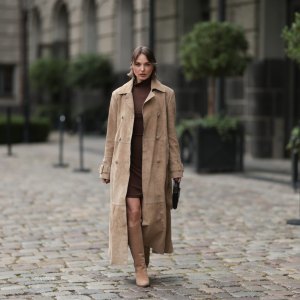 BERLIN, GERMANY - SEPTEMBER 17: Yana Pries seen wearing a long suede leather trench coat from NOUR HAMMOUR in a warm beige tone. The coat features double-breasted buttons, a structured collar, and belted cuffs, creating a luxurious yet timeless silhouette. Her hair is cut into a sleek bob, light brown with subtle highlights, styled with a middle part and softly curved ends that frame her face. Underneath she wears Even&Odd fitted chocolate-brown mini dress, with a high neckline, Bottega Veneta Andiamo clutch, a structured black leather bag with a gold knot detail on the strap and Bobbies knee-high Bobbies suede leather boots in a soft beige tone, on September 17, 2025 in Berlin, Germany. (Photo by Jeremy Moeller/Getty Images)