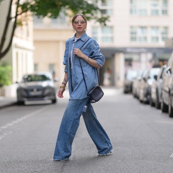 PARIS, FRANCE - JULY 17: Emy Venturini wears an oversized light blue denim shirt and wide-leg jeans, both by The Frankie Shop, layered over a white ribbed tank top by Intimissimi. Accessories include a black leather crossbody bag by Agnona, a silver Cartier wristwatch, a gold choker necklace by Vivienne Westwood, hoop earrings by Perrine Taverniti, stacked bracelets, and sunglasses by Prada. Hair is blond and styled in a center-parted low ponytail, and lips are painted with lipstick in a bold red shade, during a street style fashion photo session, on July 17, 2025 in Paris, France. (Photo by Edward Berthelot/Getty Images)