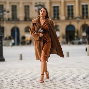 Maria Rosaria Rizzo wears golden long earrings from Raspini, a brown fluffy long winter coat from Max Mara, a brown leather monogram Vuitton bag, a brown velvet low-neck v-neck dress with lace and floral embroidery on the bottom part from Imprevu, brown high heeled shoes from Michael Kors, on December 04, 2020 in Paris, France.