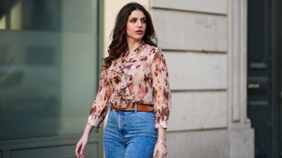 Sara Carnicella @lafillerebelle wears earrings from APM Monaco, a pink and purple floral print flowing shirt from Liu Jo, a brown leather belt from Mango, blue denim flared jeans from & Other Stories, on March 28, 2021 in Paris, France.