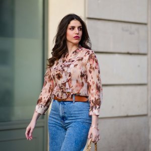Sara Carnicella @lafillerebelle wears earrings from APM Monaco, a pink and purple floral print flowing shirt from Liu Jo, a brown leather belt from Mango, blue denim flared jeans from & Other Stories, on March 28, 2021 in Paris, France.