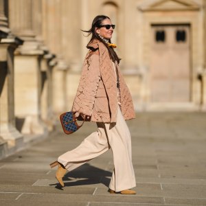 Alba Garavito Torre wears pearls earrings, black wayfarer sunglasses from Ray Ban, a beige quilted oversized jacket from Munthe, a white and yellow silk scarf tie with classic knot from Lollys Laundry, a brown / beige braided wool pullover from Polo Ralph Lauren, a brown shiny leather belt, high waist beige palazzo pants from Bimba y Lola, a blue denim monogram and brown shiny leather Jackie 1961 Mini bag handbag from Gucci, yellow mustard suede block heels ankle boots, gold bracelets, gold rings, during a street style fashion photo session, on November 12, 2021 in Paris, France.